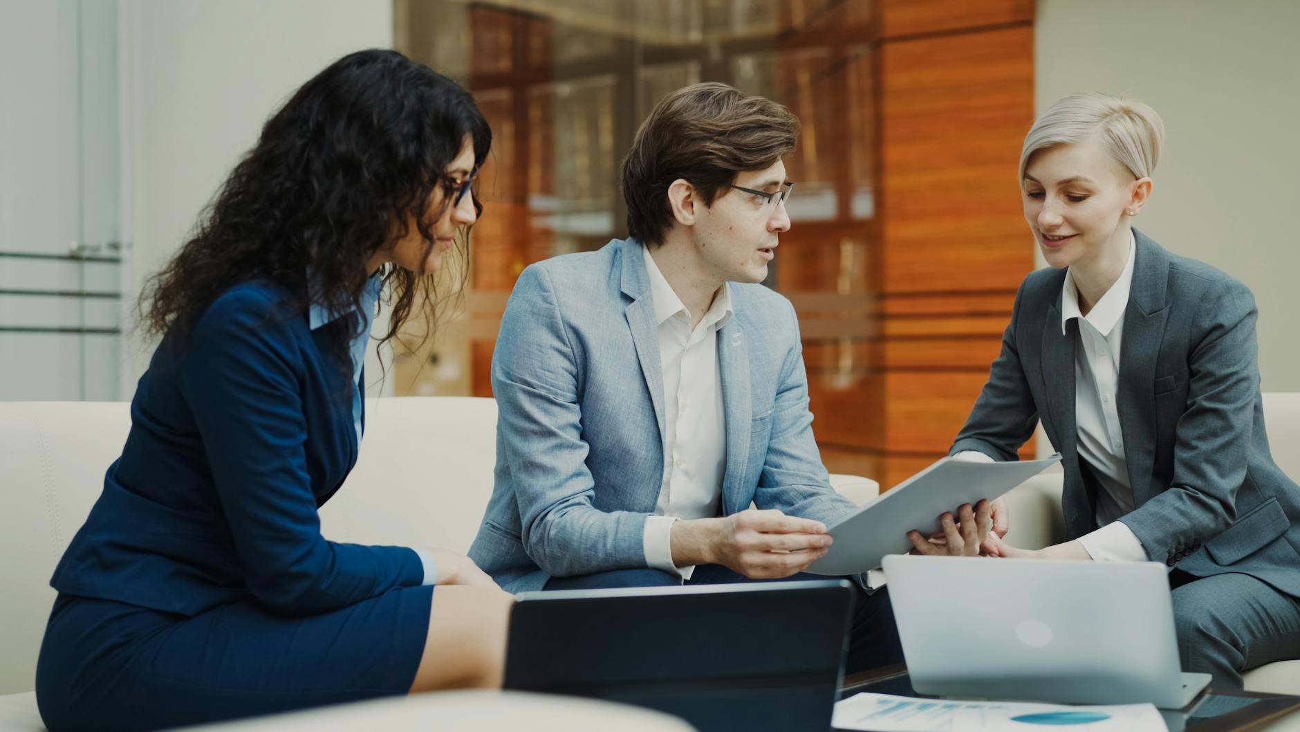 Three professionals discussing over a tablet in a modern office setting.