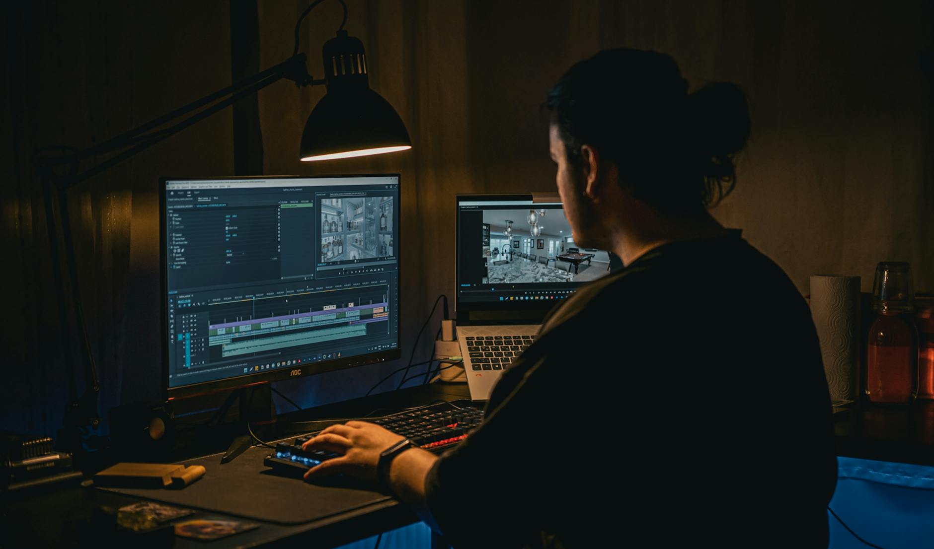 A man works at a computer editing video footage in a dimly lit workspace.
