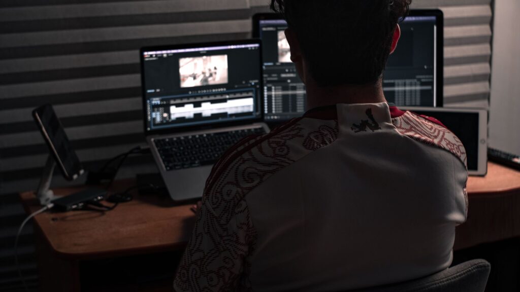 Man sitting at desk working on video editing software with dual monitors in an office.